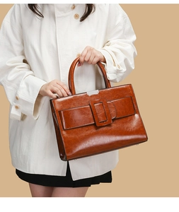Close-up of brown glossy oil wax leather handbag featuring a vintage buckle and round handle