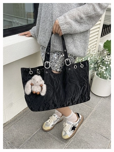 Detail of a large black tote bag with silver eyelets and a plush white bunny charm