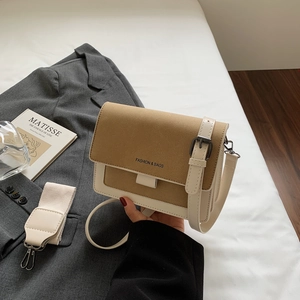 Borsa a tracolla retrò bicolore in pelle con tracolla larga su sfondo di letto bianco