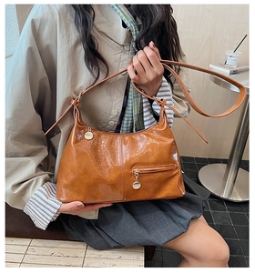 Detail of caramel pleated faux leather hobo bag with gold metal pendant in a cafe setting