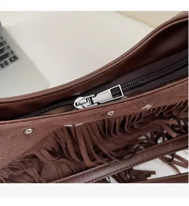 Nahaufnahme des Reißverschlusses an der braunen Wildledertasche mit Fransen und Nieten