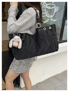 Detail of a large black textured tote bag with silver grommets and plush bunny charm