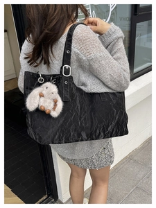 Macro shot of black textured tote bag with a white rabbit plush charm on a grey sweater