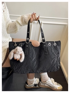 Close-up of black wrinkled leather tote bag with a plush rabbit charm and silver metal rings