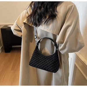 Detail of black crescent shoulder bag with pearl bead texture on a model outfit