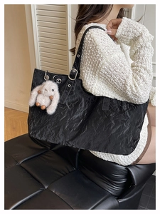 Detailed side view of black pleated tote bag with plush bunny charm on leather strap