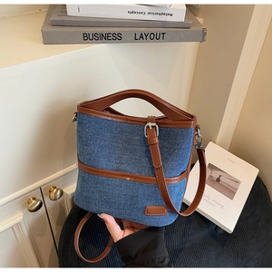 Detail of blue denim bucket bag with brown leather trim and metallic buckle closure