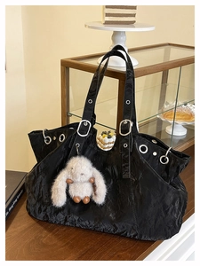 Detail of black textured tote bag with silver eyelets and a plush bunny charm on wood counter