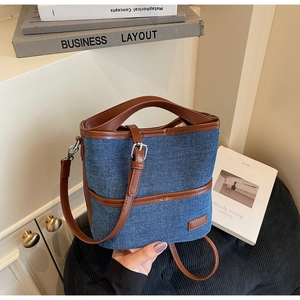 Detail of blue denim bucket bag with brown leather handles and adjustable strap