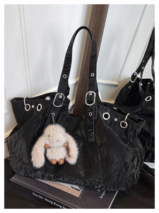 Detail of black pleated tote bag with silver eyelets and white plush bunny charm