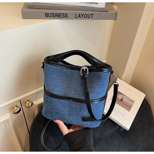 Close-up of blue denim bucket bag with black leather handles and silver hardware