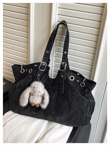 Detail of black tote bag with pleated texture, silver eyelets and a plush rabbit charm