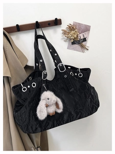 Detail of black pleated tote bag with silver eyelets and a plush rabbit charm decoration
