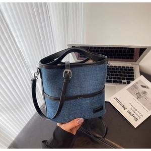 Detail of denim bucket bag with black trim, styled with a laptop and design books