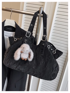 Detail of black wrinkled tote bag with silver metal eyelets and a plush rabbit charm
