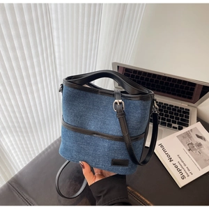 Detail view of blue denim bucket bag with black leather handle and strap on a desk