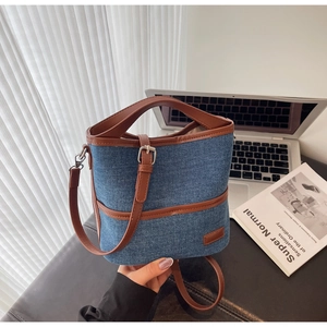 Detail of denim bucket bag with brown faux leather trim beside a laptop