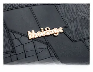 Detail of black faux crocodile leather texture and golden metal logo on the handbag