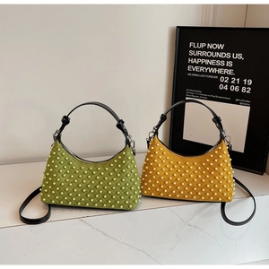 Close-up of green and yellow quilted suede handbags with pearl embellishments on marble