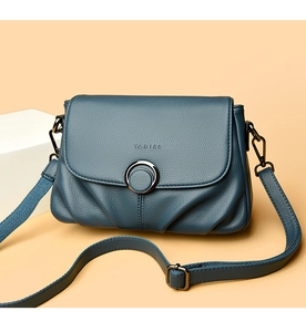Close-up of pebble leather texture and round metal buckle on a deep blue crossbody bag