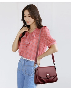 Detailed close-up of wine red textured leather handbag with gold circular metal buckle