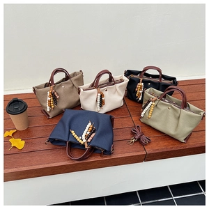 Detail view of canvas handbags in five colors with beads and leather trim on a bench