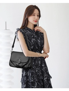 Detail of black pebbled leather shoulder bag with silver ring on floral dress model