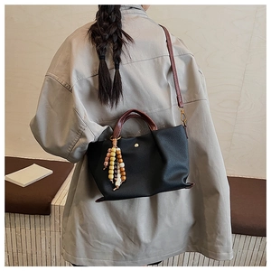 Close-up of black pebbled leather tote with ethnic beaded tassel charm and brown handle