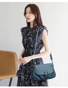 Detail of dark green leather shoulder bag with round metal buckle and embossed logo