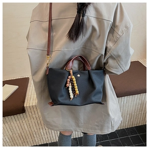 Detail of black pebbled leather tote bag with brown handles and colorful wooden bead charms