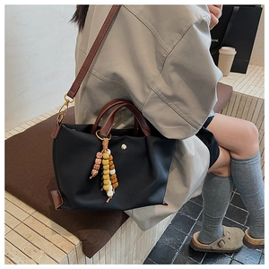 Detail of black canvas tote bag with leather straps and colorful beaded charm accessory