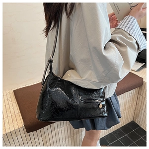 Close-up of black glossy crinkled texture on shoulder bag with metallic zipper and pendant