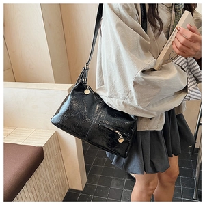Close-up of black glossy crinkle texture shoulder bag with gold metal zipper puller