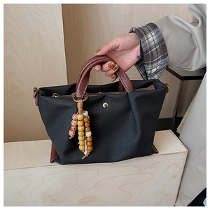 Detail of black canvas tote featuring brown leather handles and decorative wood beads
