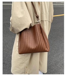 Close-up of brown woven bucket bag featuring detailed knot strap on a leather shoulder bag