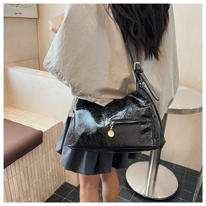 Detail of black patent leather shoulder bag with wrinkled texture and gold zipper