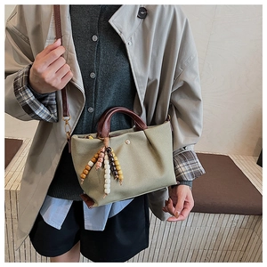Close-up of green canvas tote with snakeskin leather handle and bohemian shell tassel