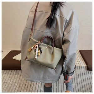 Close-up of olive green canvas tote bag with brown leather handles and bead charm detail