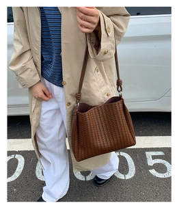Detail of dark brown woven shoulder bucket bag worn by model in a daily commuting scene