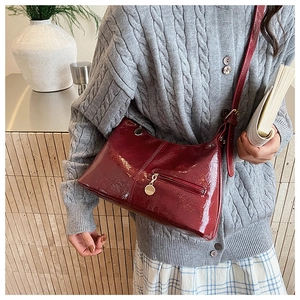Detail of burgundy glossy leather shoulder bag with sleek metal zippers and refined texture