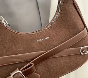 Détail d'un sac demi-lune en daim marron avec des brides en cuir et un zip argenté.