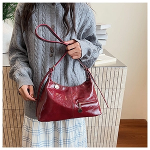 Detail of red glossy hobo bag with round metal charm and functional front pocket