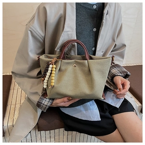 Close-up of green canvas handbag with brown leather handles and decorative wood beads