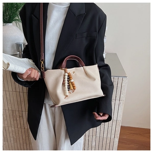 Detail of beige canvas handbag featuring a wooden bead tassel and brown leather handles