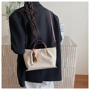 Detail of cream leather tote bag with tricolor wood bead tassel on black blazer