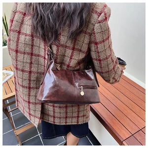 Close-up of wine red vintage leather shoulder bag with metallic pendant and zipper detail