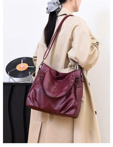 Detail shot of a large burgundy PU leather shoulder bag with silver rivets worn by a model