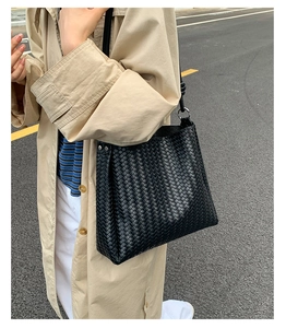 Detail of black woven leather tote bag with metallic ring held by a model in a trench coat