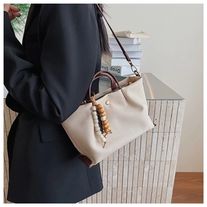 Detail of canvas tote bag with brown leather trim and decorative beads on a model