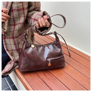 Close-up of vintage dark brown glossy wrinkled leather handbag with gold metal charm